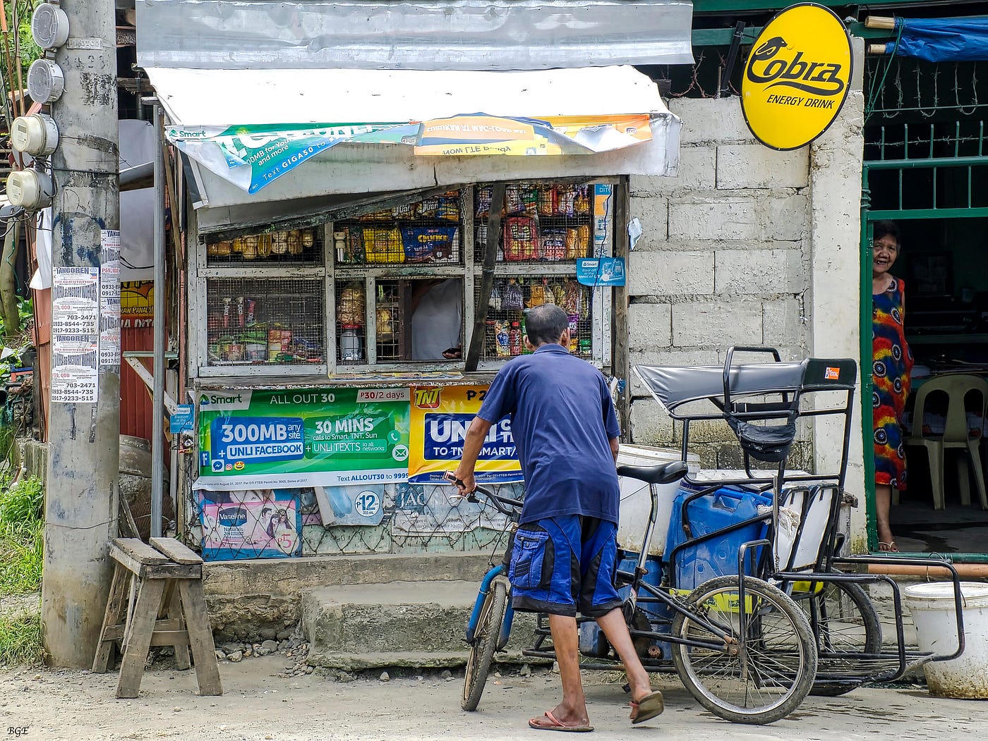 Corner sari-sari with cola fascia, noodle tarp and a passing jeepney.